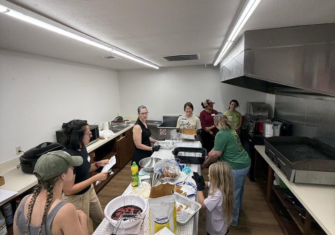 Group of people in a kitchen preparing food, with a child and various kitchen items on the counter.