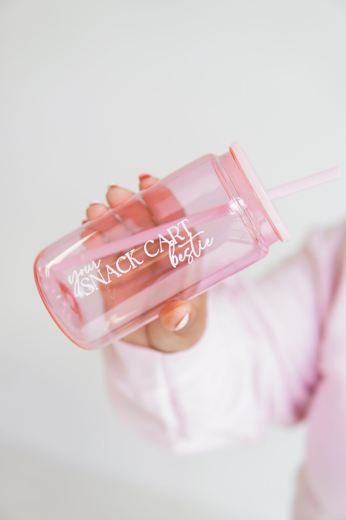 Person holding a pink transparent water bottle with a straw, text on bottle reads 'You can't buy happiness'.