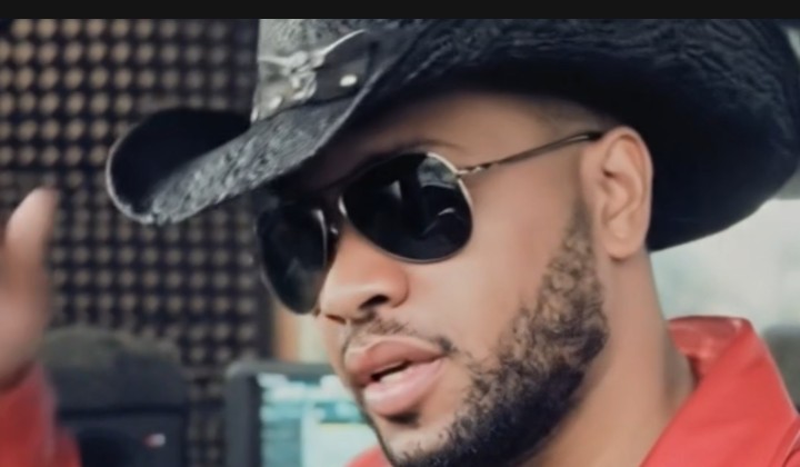 Man wearing sunglasses and a wide-brimmed hat, with a beard, outdoors, with a blurred background.