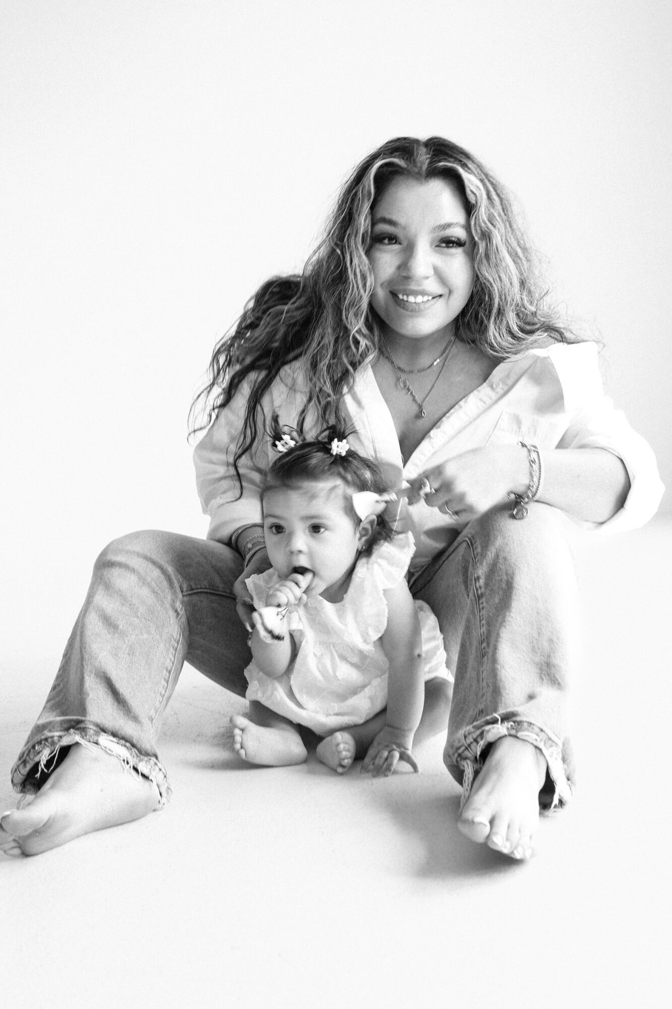 Woman and child sitting on the floor, smiling, in a studio with a plain background.