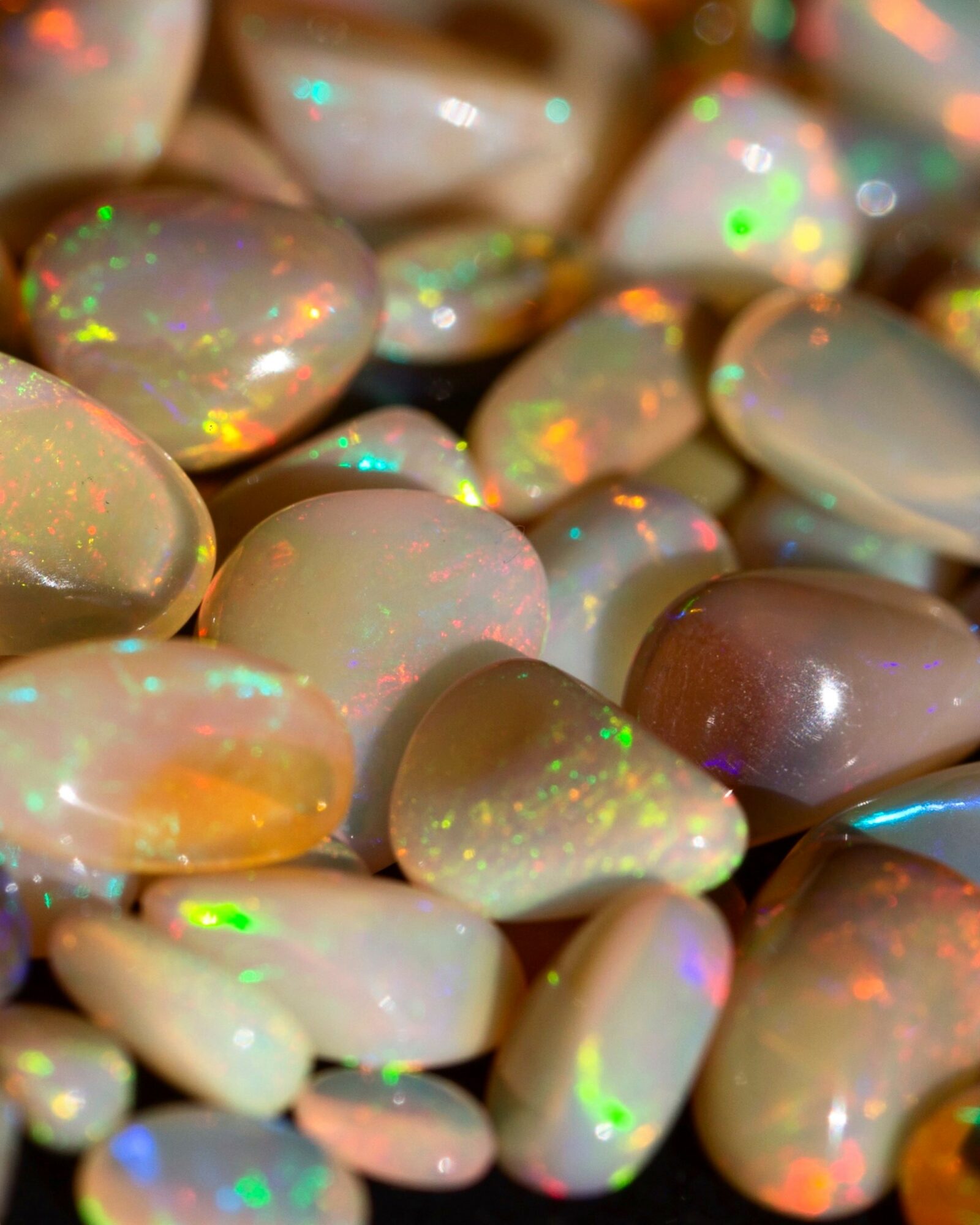 Close-up of smooth, oval-shaped opal stones with colorful iridescence and glow.