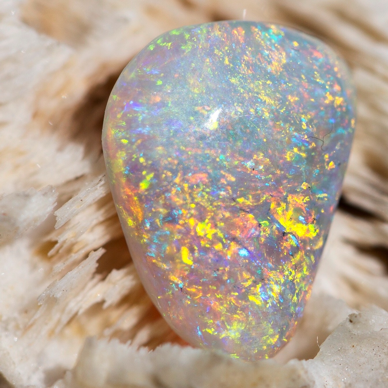 Close-up of an opal gemstone with vibrant rainbow colors, resting on a textured, light-colored surface.