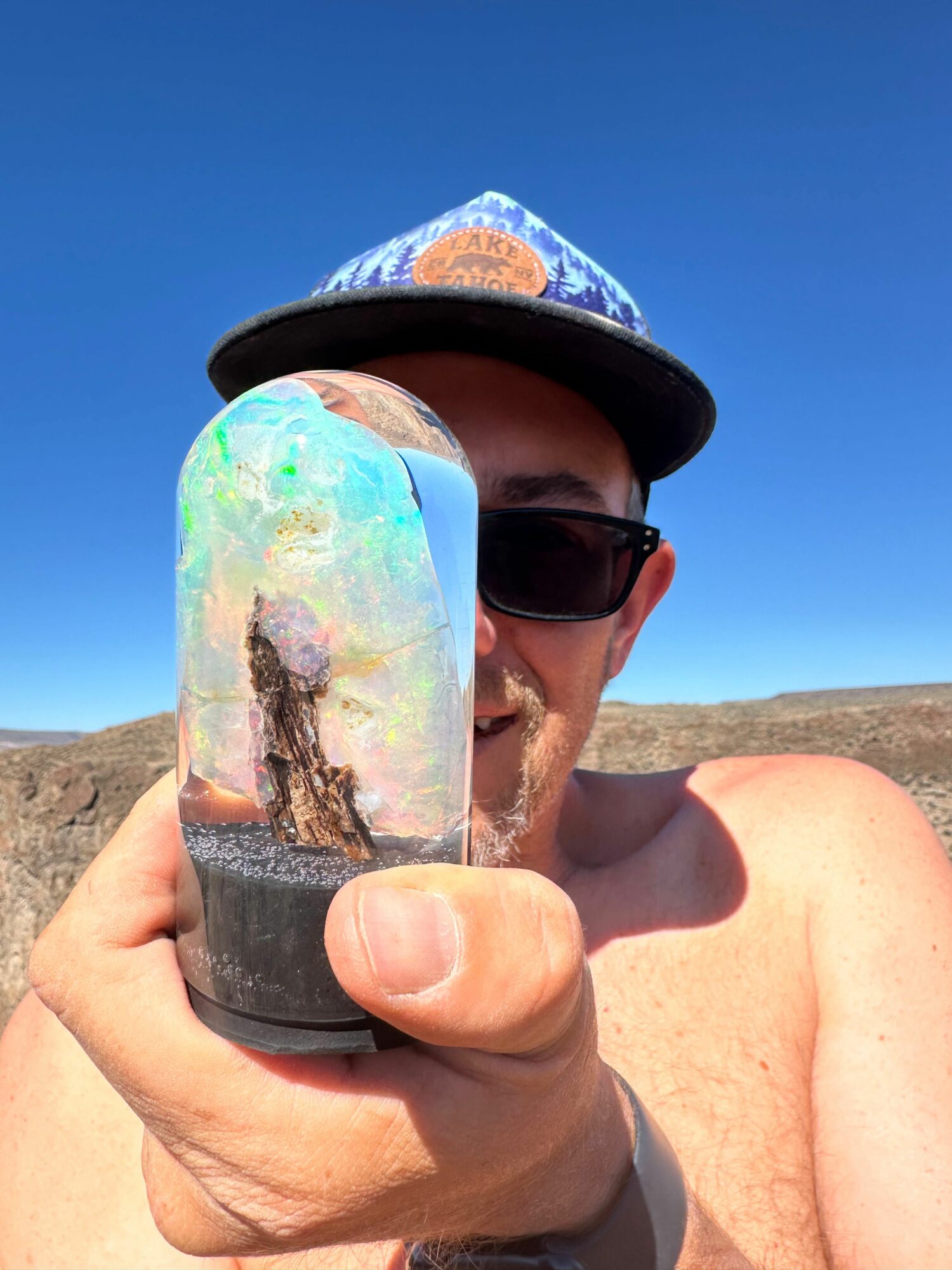 Person holding a colorful drink in a clear cup outdoors with a blue sky background.