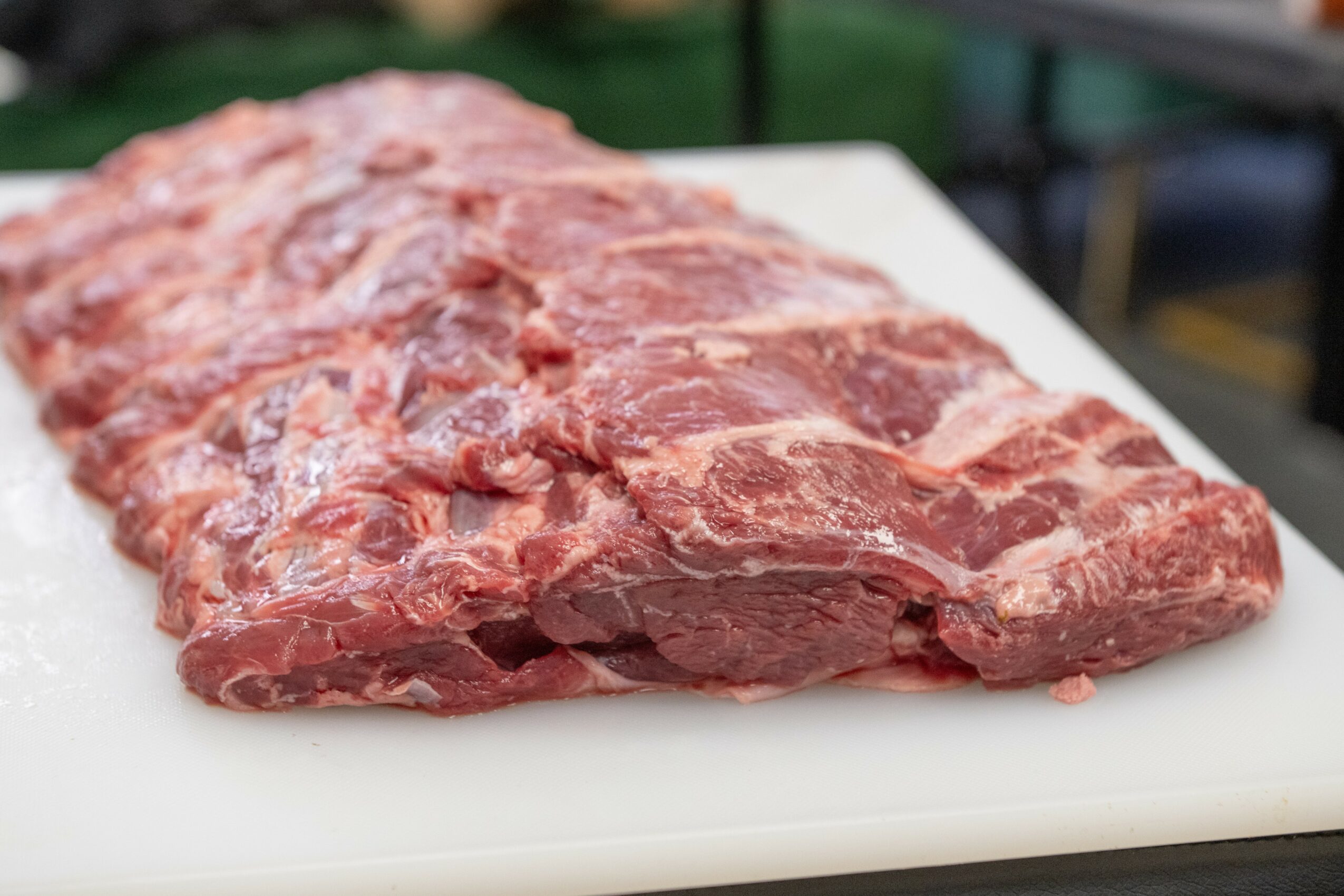 Raw meat cut on a white cutting board with a blurred background, close-up view.