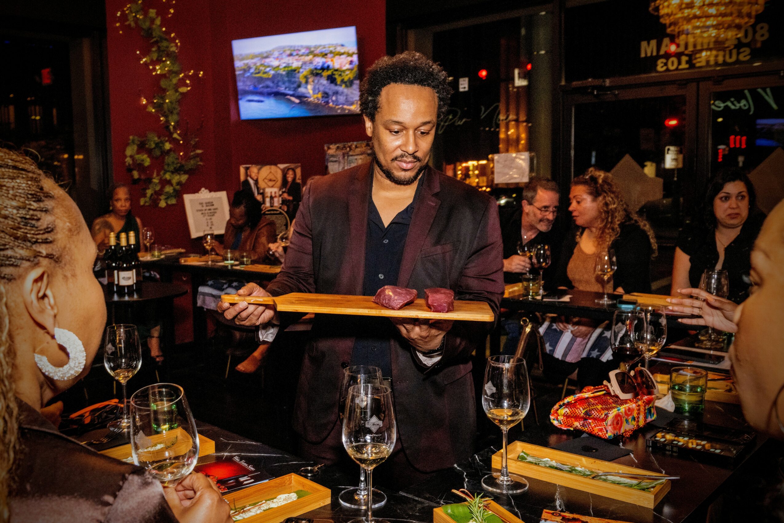 Bartender serving drinks at a lively bar with people socializing, colorful decor, and a television screen in the background.