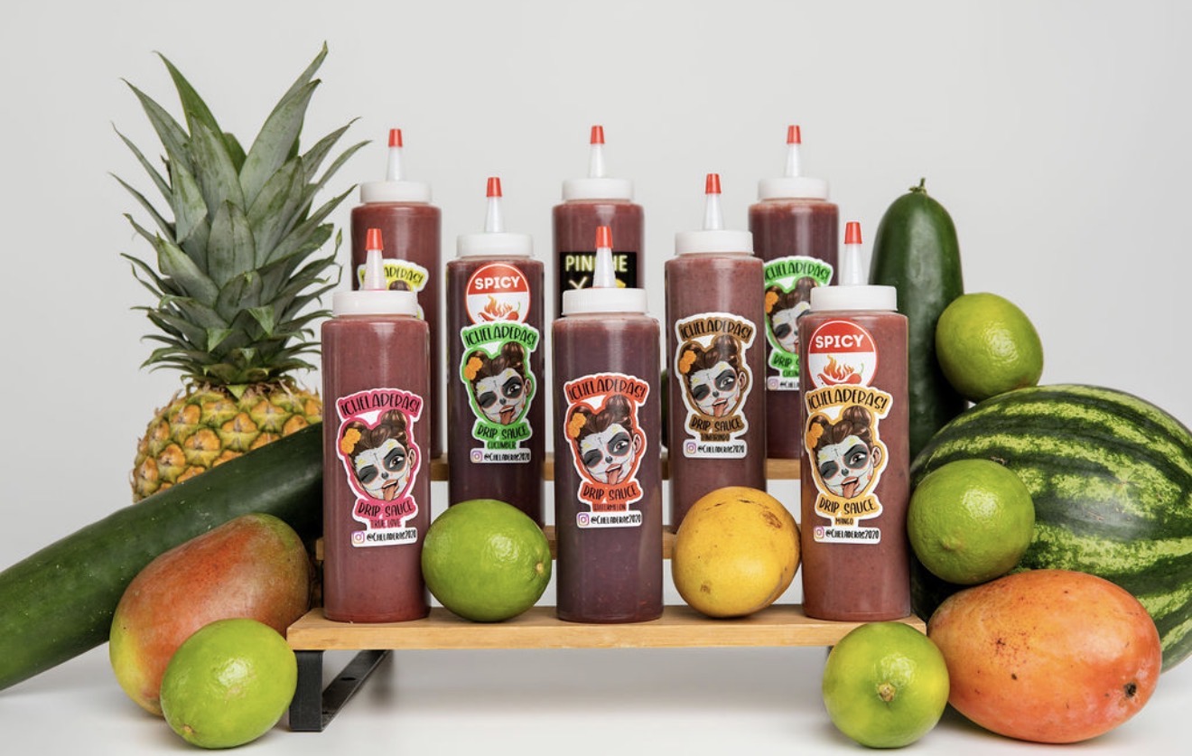 Pineapple, watermelon, mango, limes, and bottles of sauce with cartoon labels on a white surface.