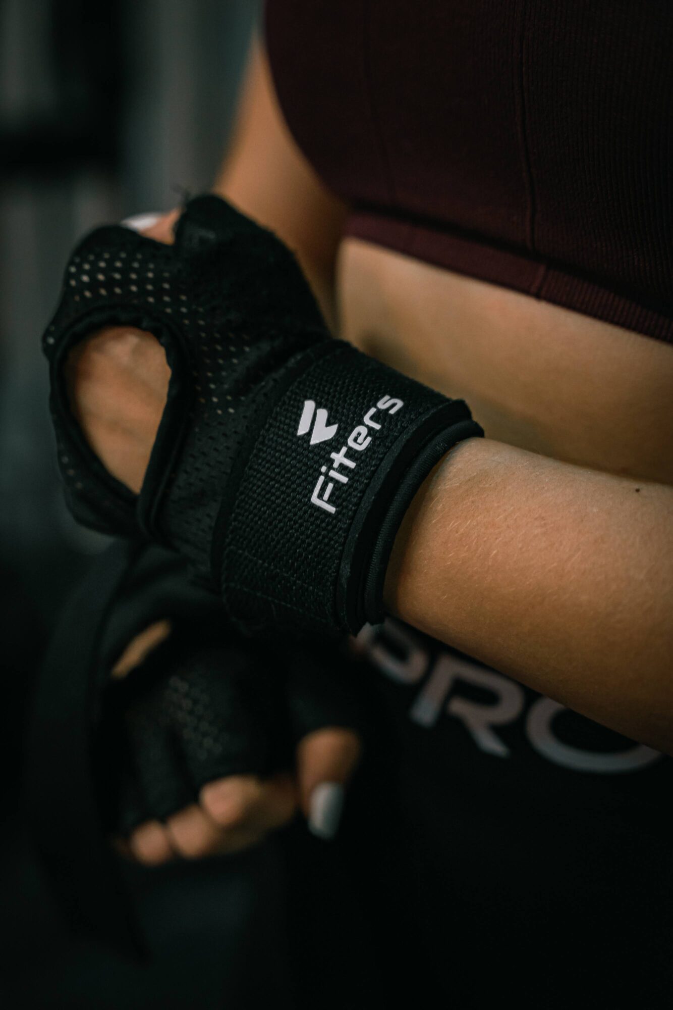 Person wearing a black fitness glove with white text, holding a dumbbell, in a gym setting, cropped image.