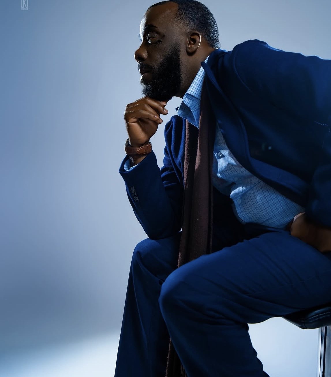 Man in suit sitting with hand on chin, looking thoughtful, against a plain background.