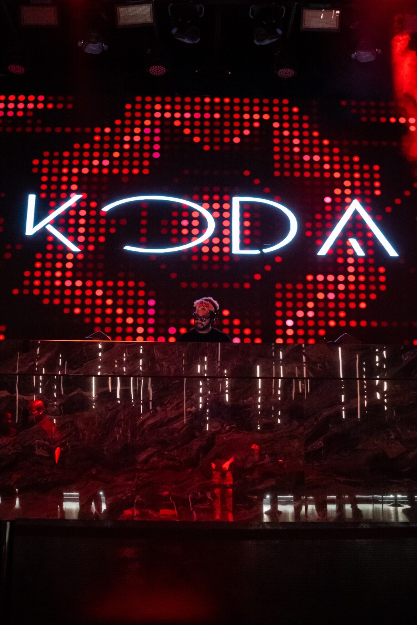 Stage with large illuminated sign displaying 'KDA' and a red dotted background, with reflections on the floor.