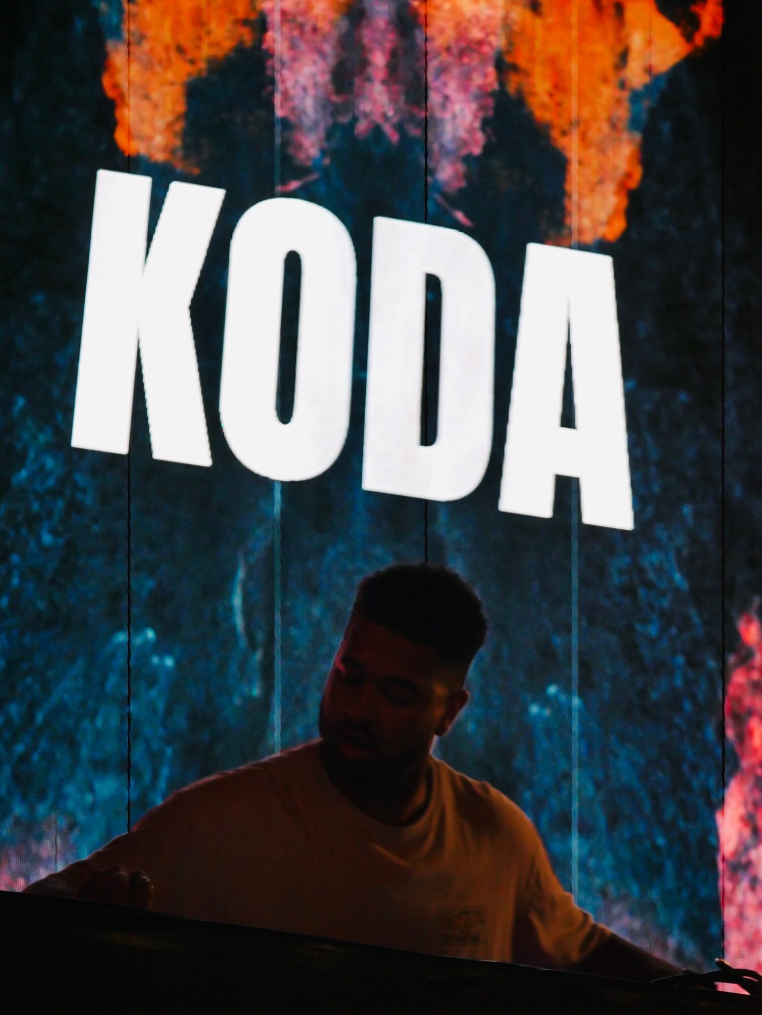 Person performing on stage with colorful background and large white text reading 'KODA'.