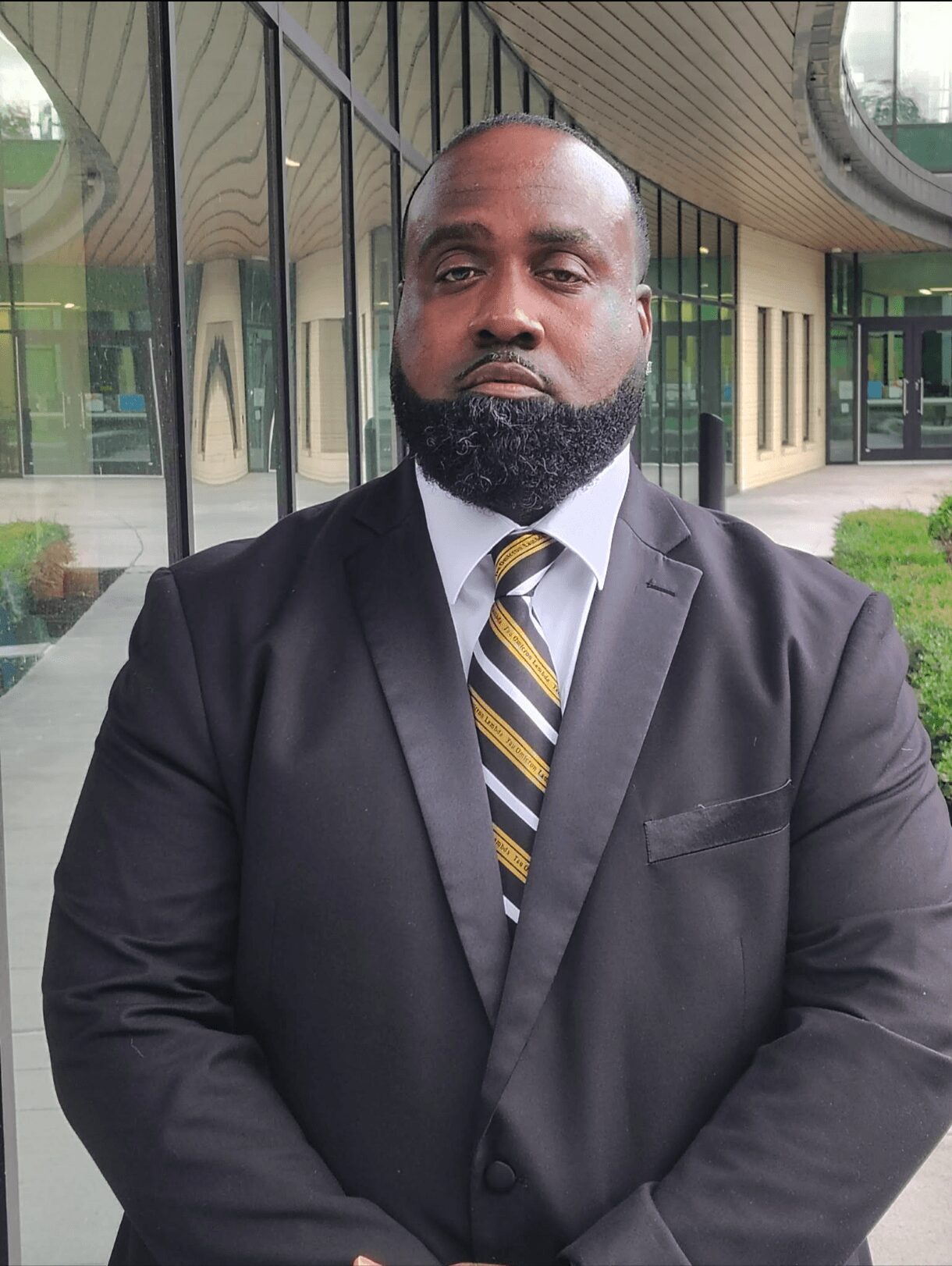 Man in a suit with a striped tie standing outside a modern building with glass windows.