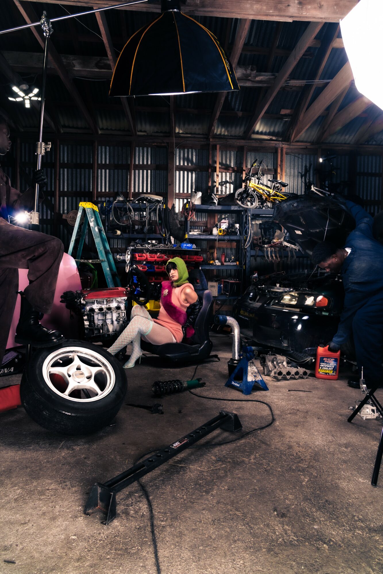 Workshop with tools, car parts, and a person working, cluttered space with a tire and equipment visible.