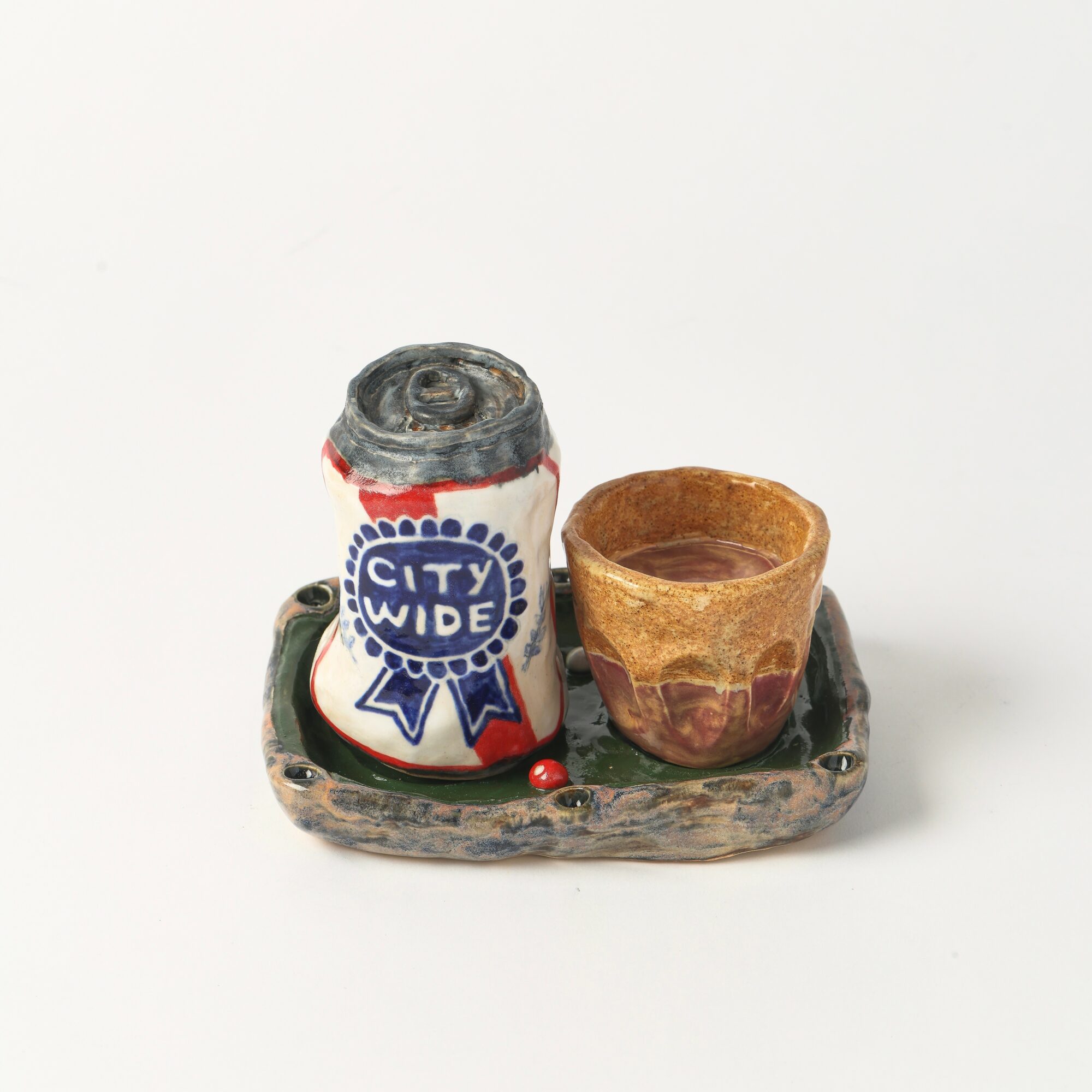 Small ceramic tray holding a decorated can and a small clay cup, on a white background.