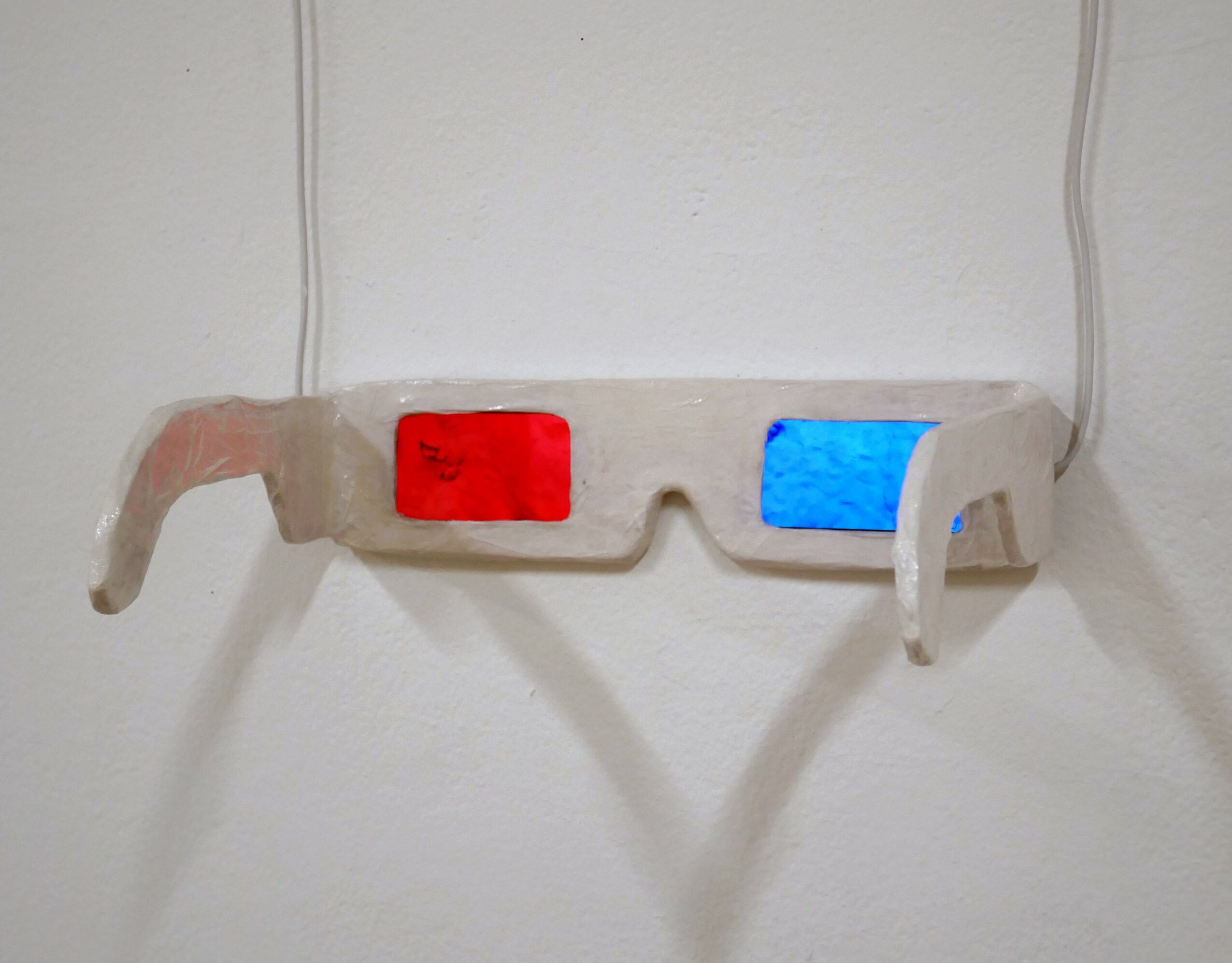 Eyeglasses with red and blue lenses hanging on a wall, casting shadows.