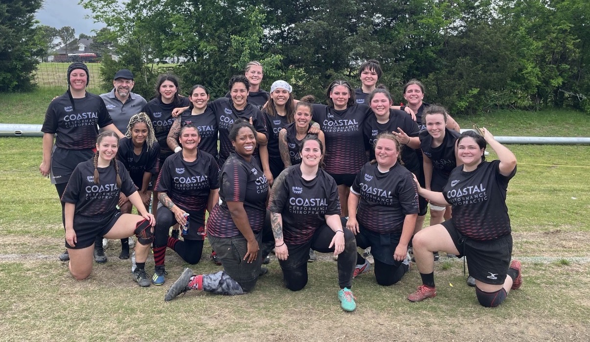 Group of women in matching sports uniforms outdoors on grass, smiling and posing for a team photo.