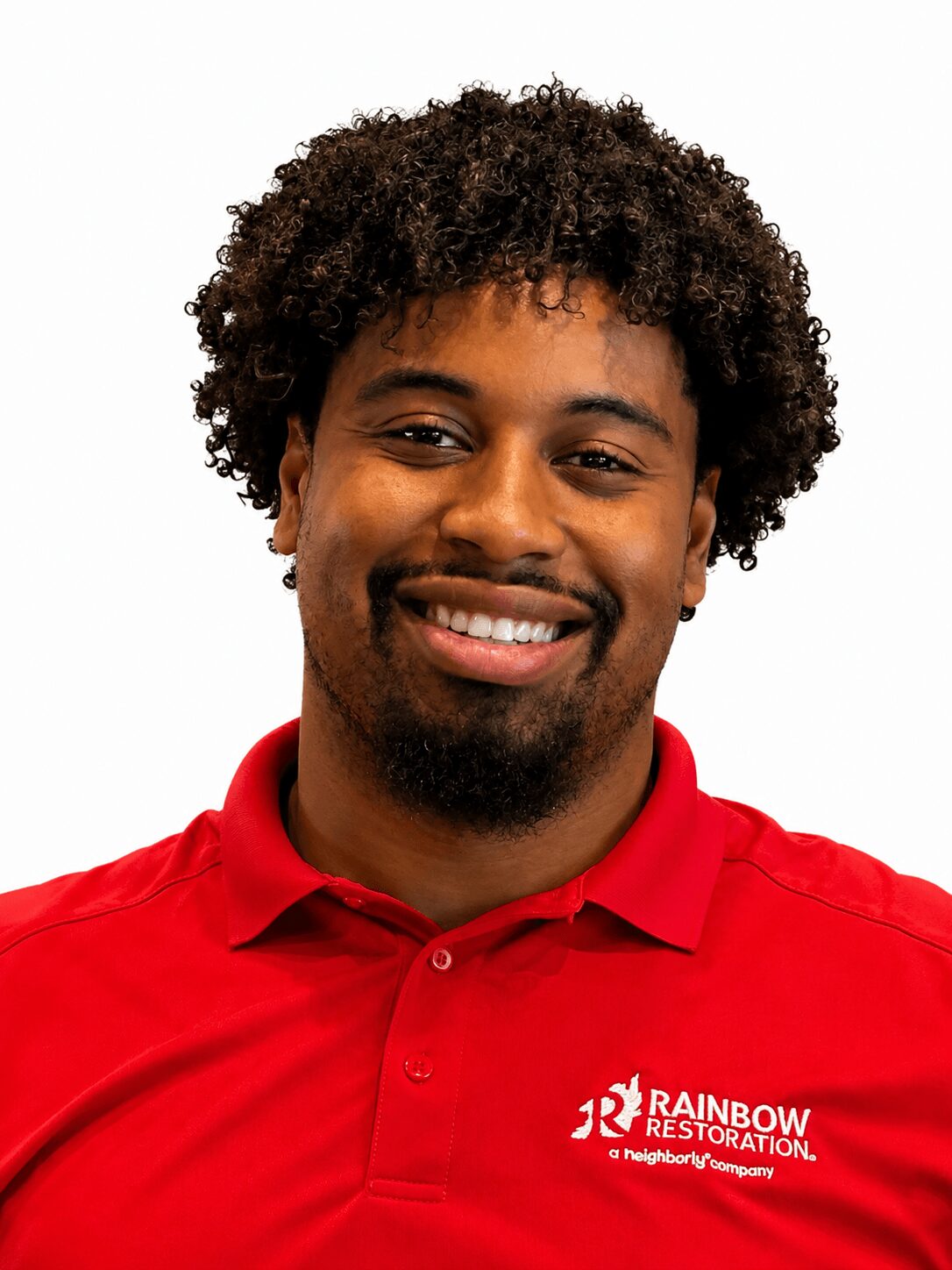 Smiling man with curly hair wearing a red polo shirt with a logo, against a white background.