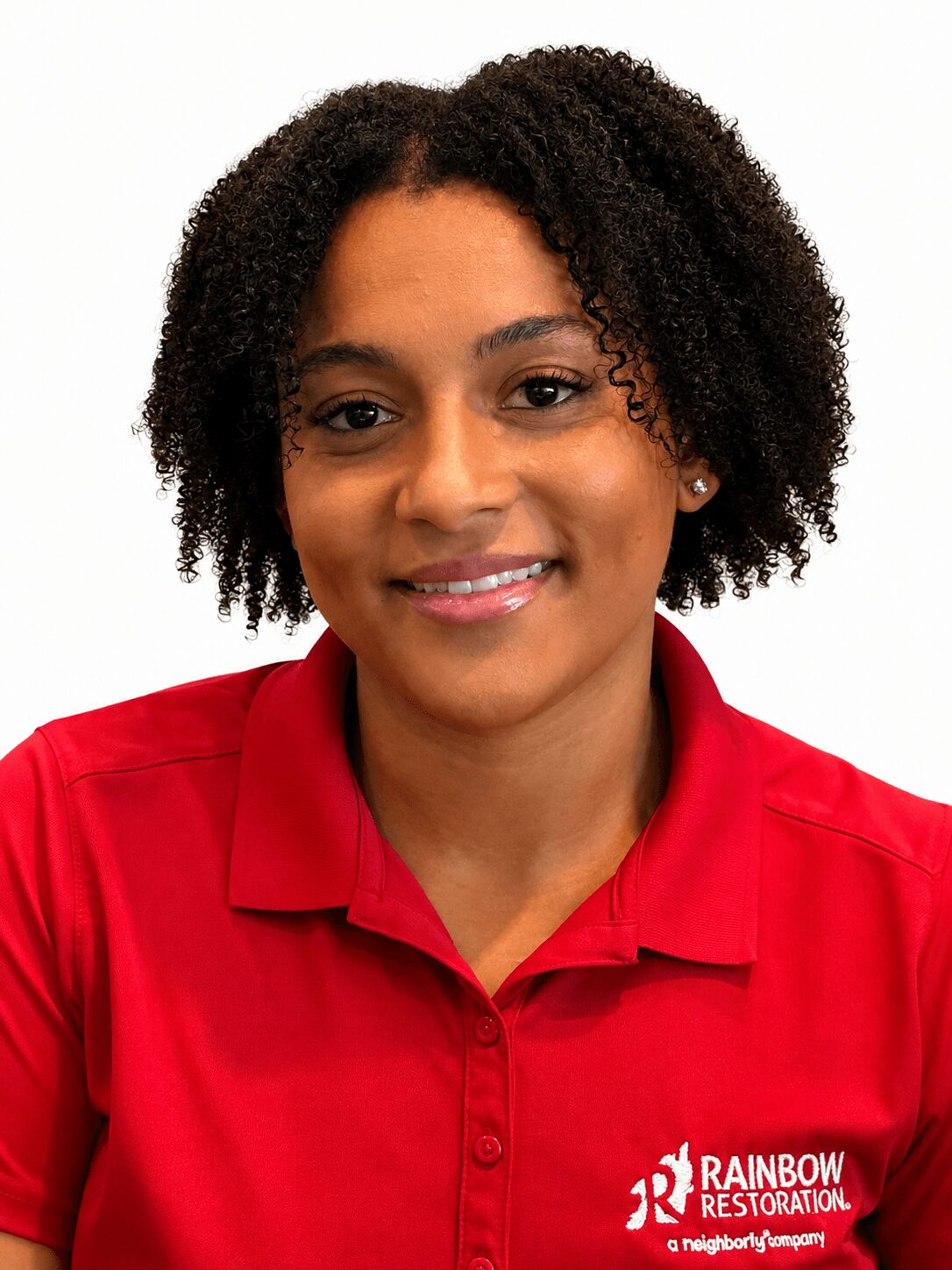 Woman with curly hair wearing a red polo shirt, smiling, against a white background.