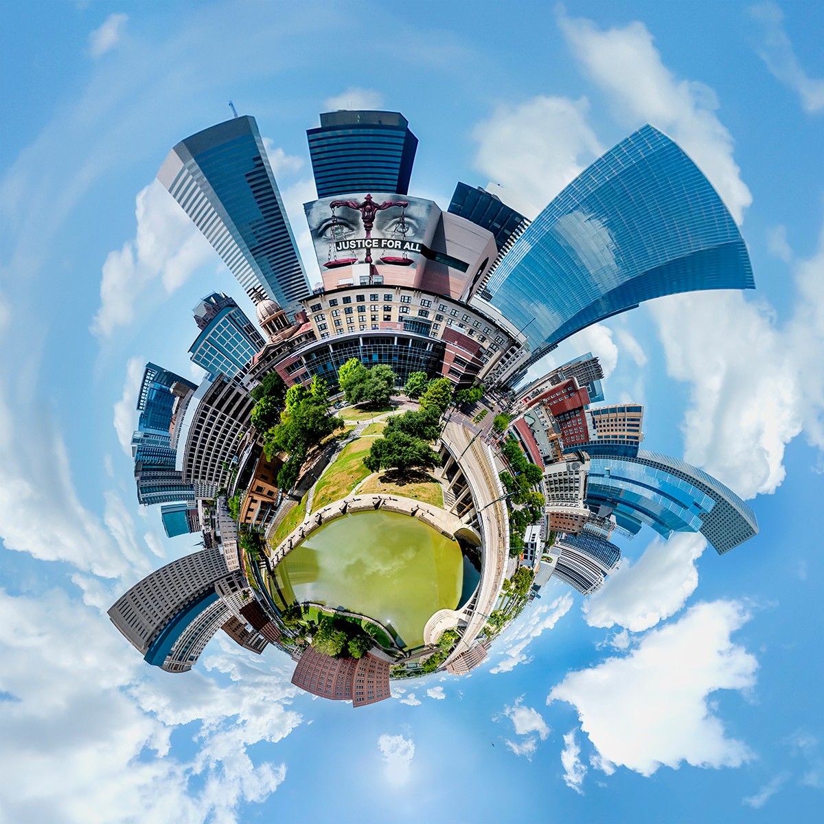 Panoramic view of a city park with water, surrounded by tall modern buildings, under a partly cloudy sky.