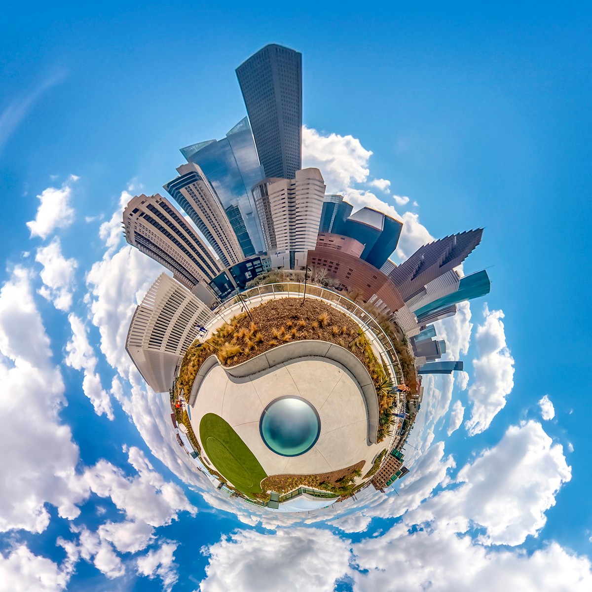 Panoramic view of a cityscape with tall buildings, a circular park, and a blue sky with clouds.