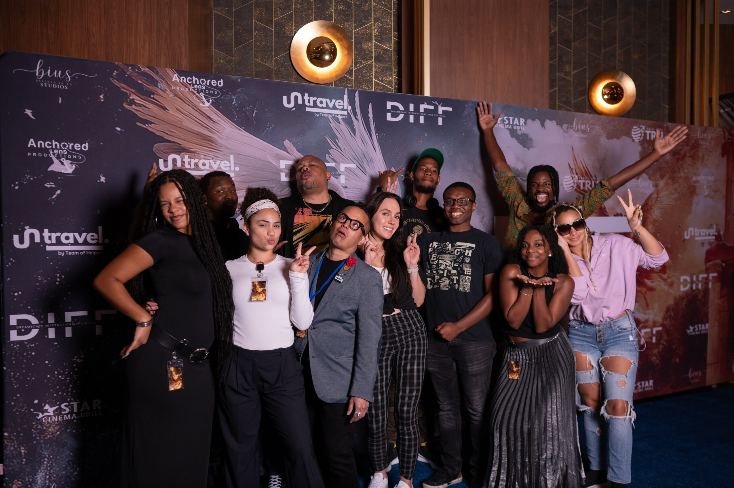 Group of people posing in front of a backdrop at an event, some making gestures and smiling.
