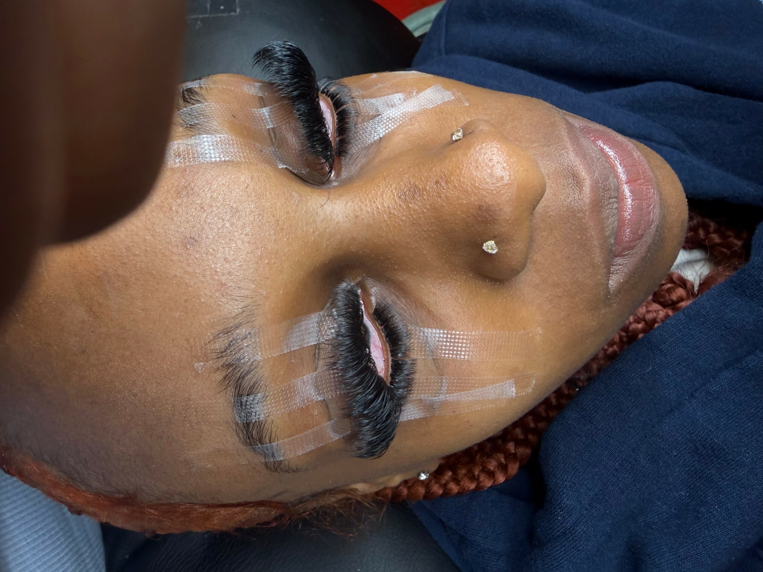 Close-up of a person's face with makeup, lying down with eyes closed, showing detailed eye makeup and facial features.