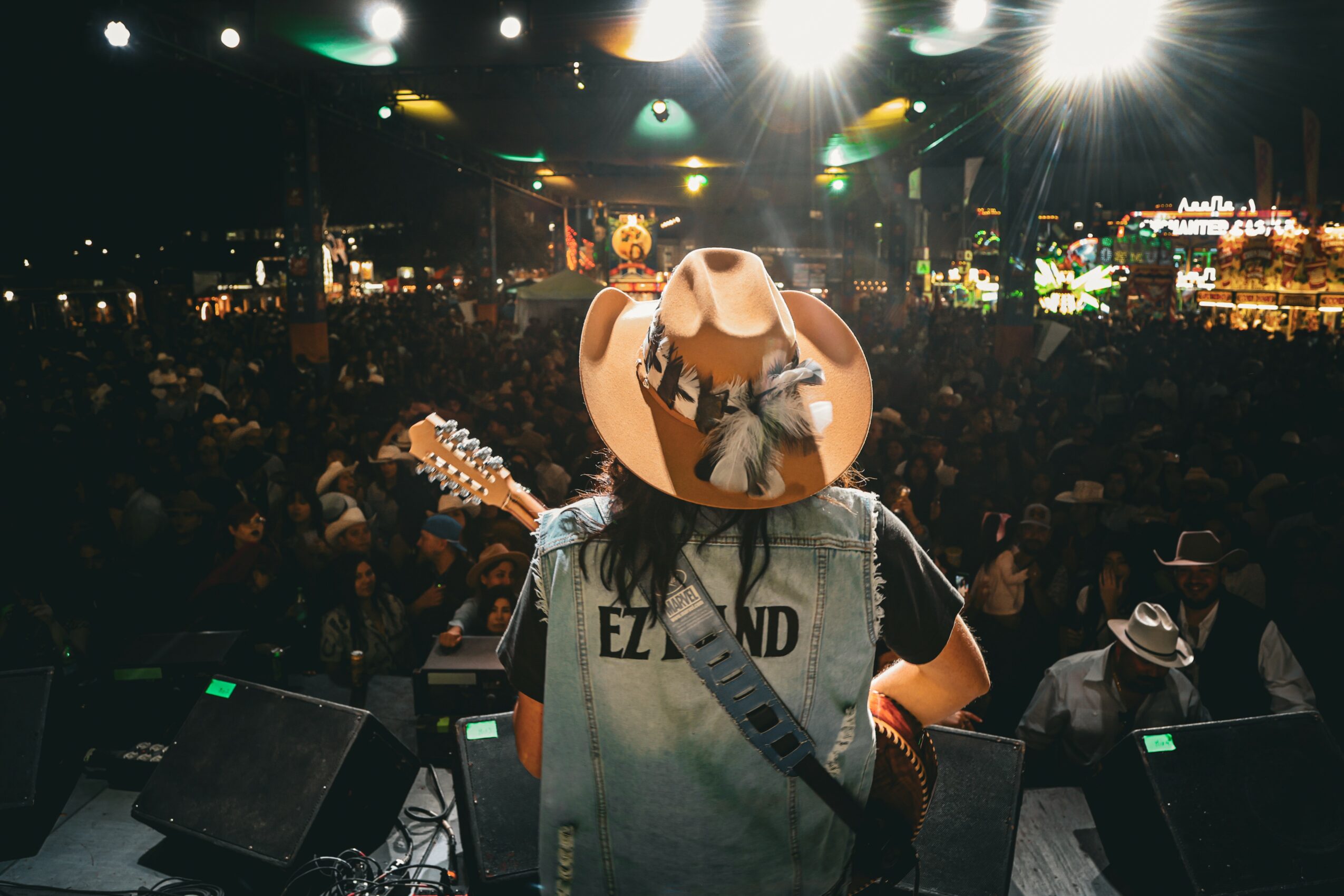 Person wearing a cowboy hat and a gray T-shirt with a crowd and stage in the background.