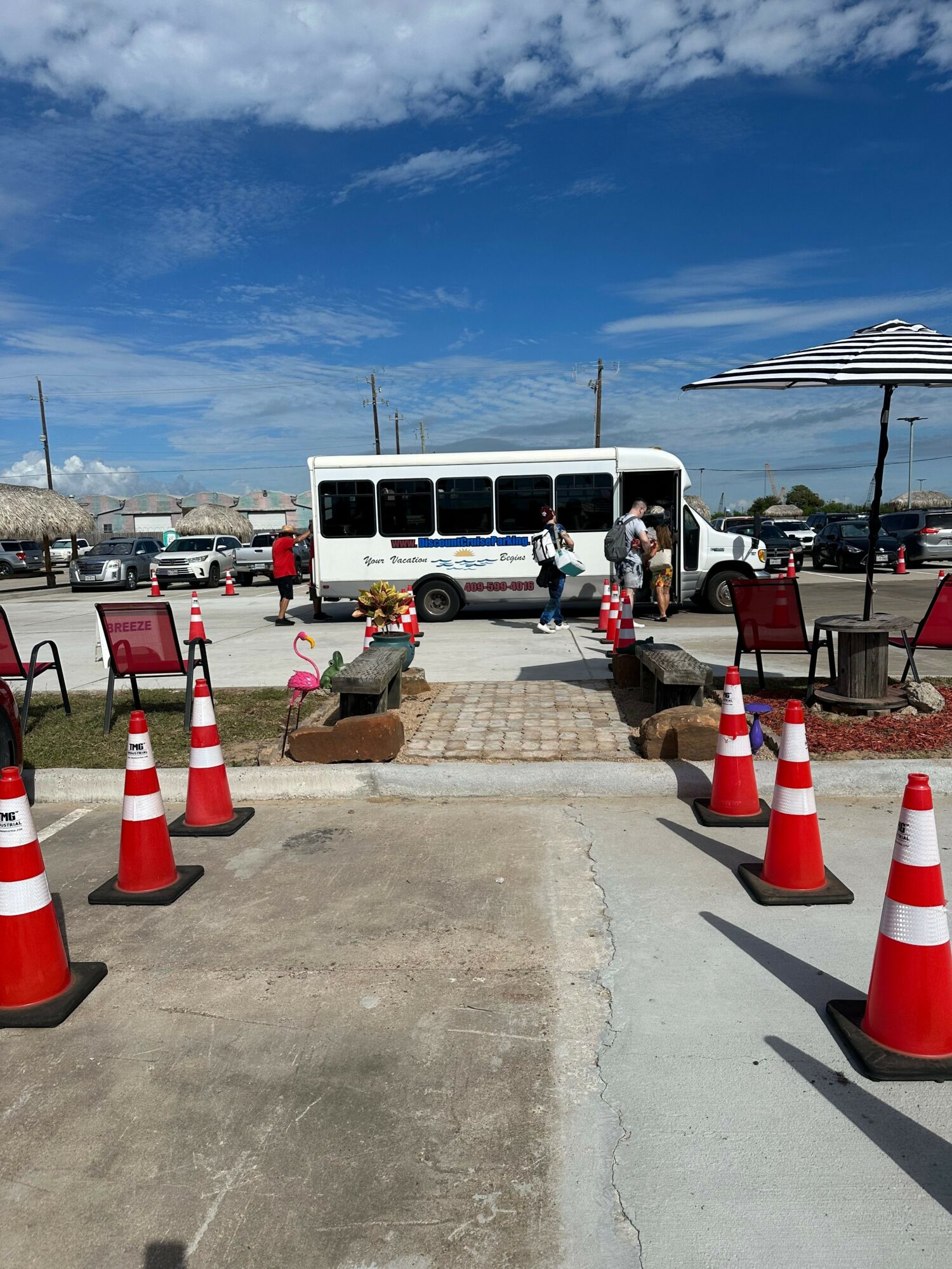 People working on a sidewalk with orange traffic cones, near a boat docked at a marina under a blue sky.