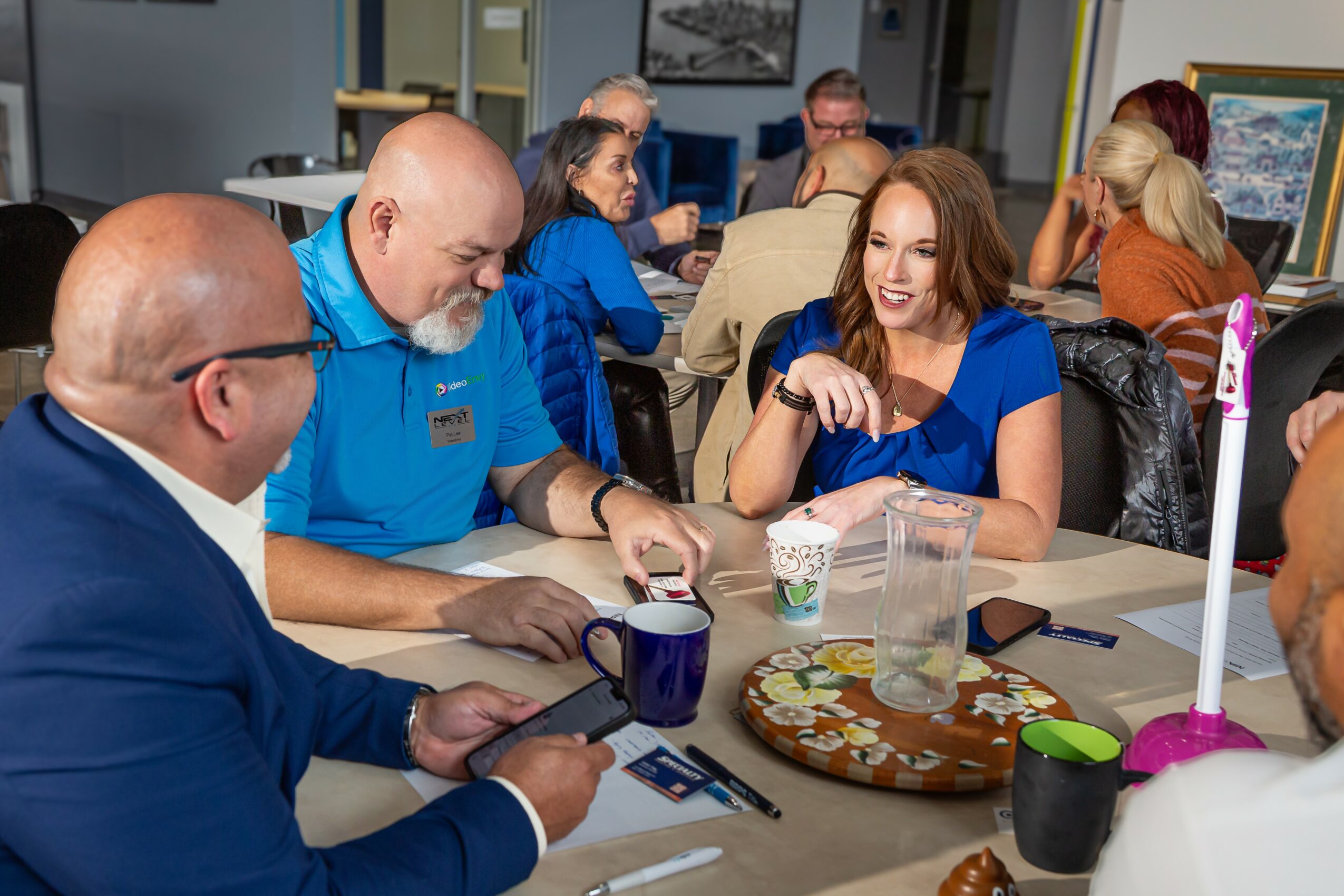 Group of people in a meeting room, engaging in conversation, with laptops and drinks on the table.