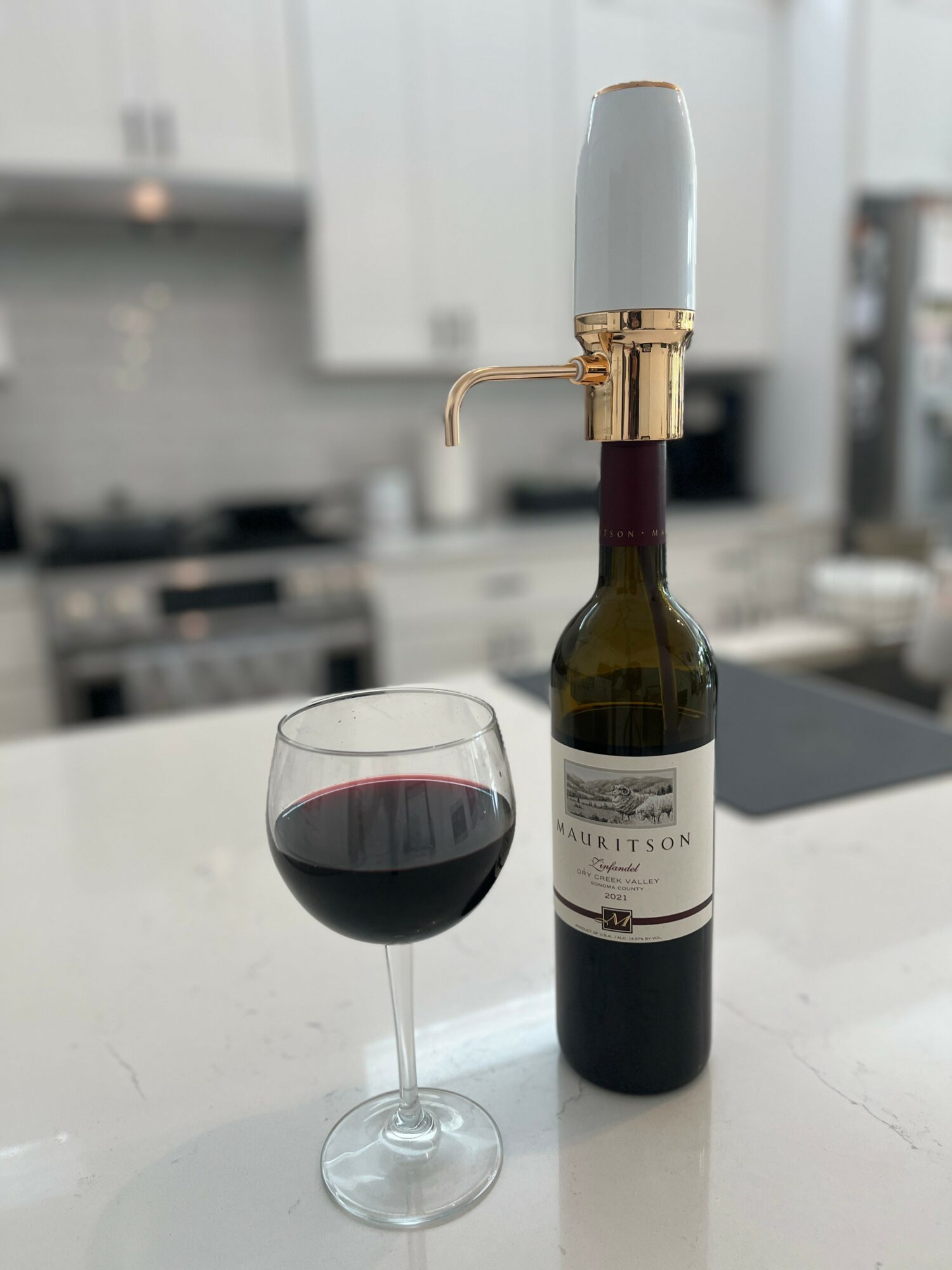 A wine bottle with a spout and a glass of red wine on a white countertop in a kitchen.