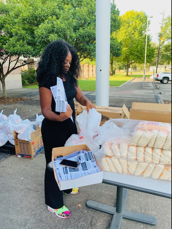 Woman with curly hair packing items into boxes outdoors, with trees and parked cars in background.