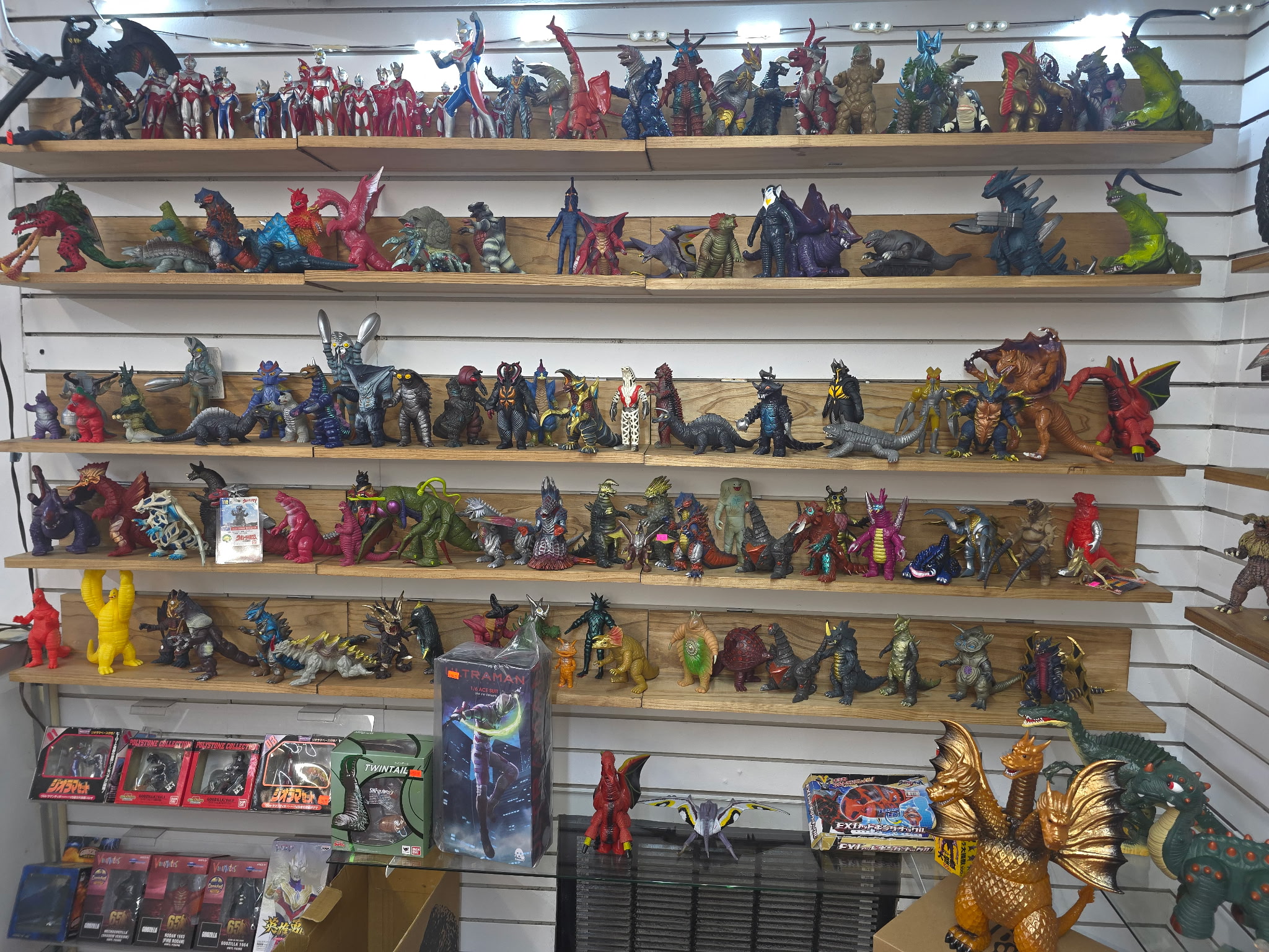 Display of various colorful toy figures on shelves, including animals, superheroes, and vehicles, with some packaging visible at the bottom.
