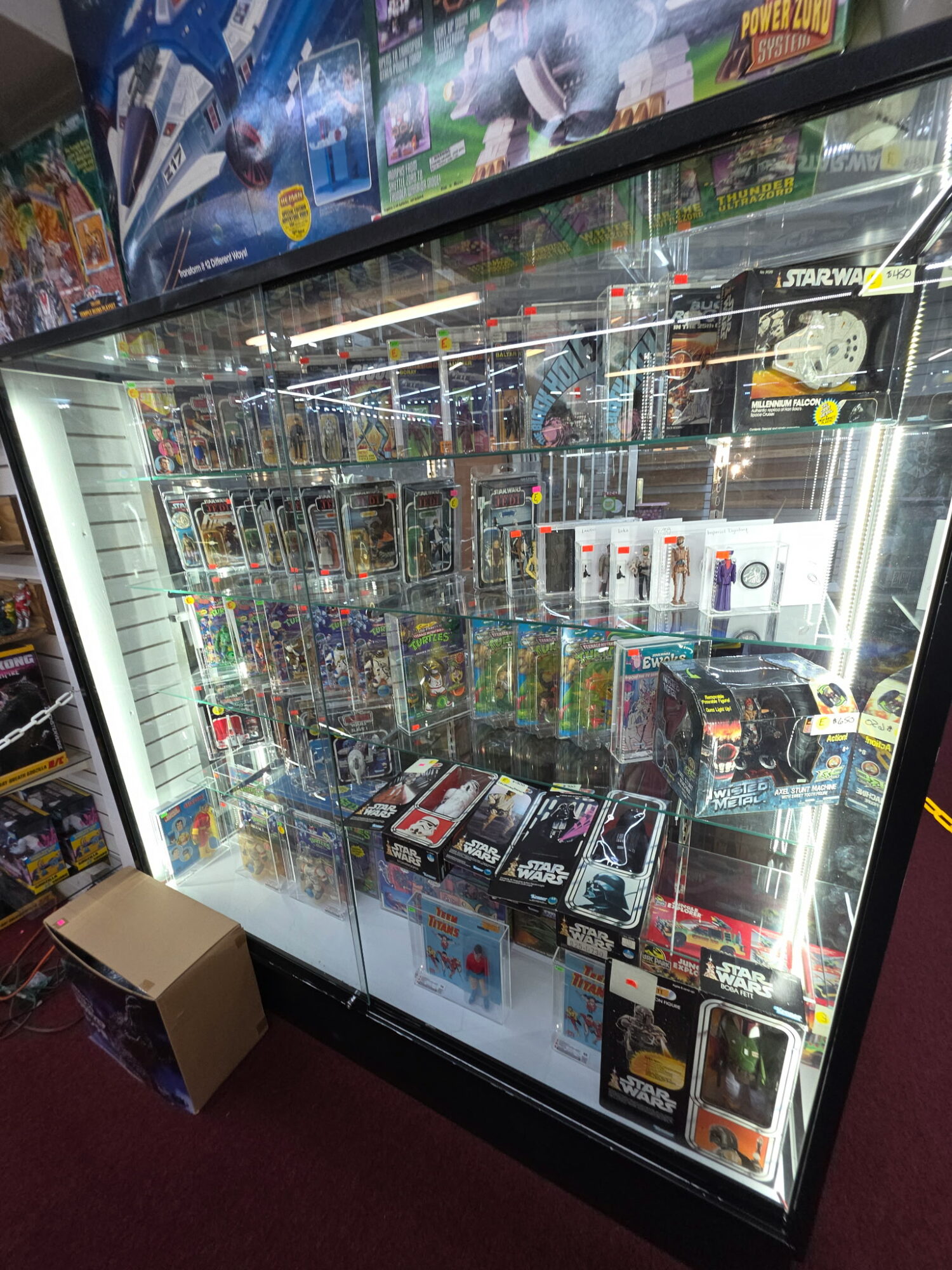 Display case filled with various toys and collectibles, shelves packed with boxed items, in a retail store.