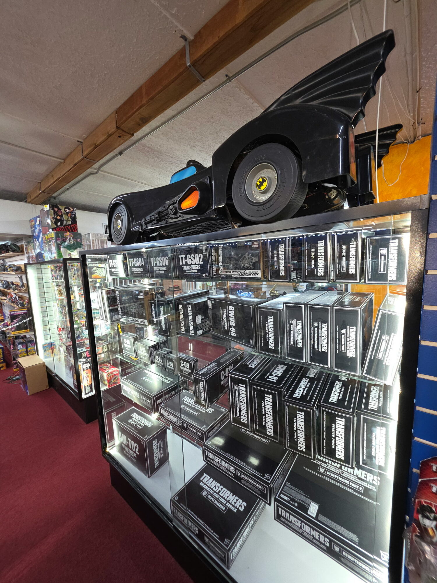 Display case filled with boxed items, a black speaker on top, and a wooden ceiling beam above.