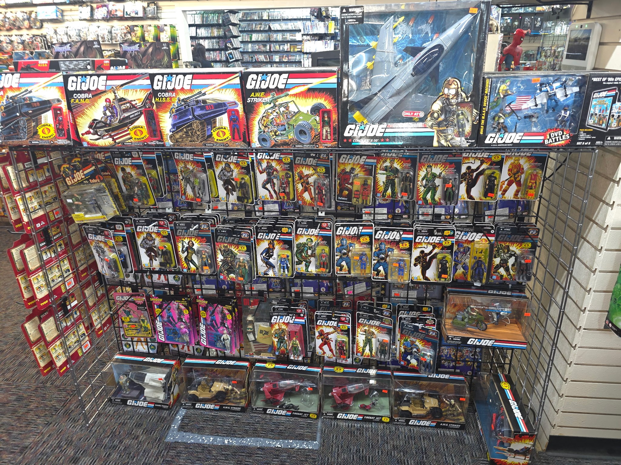 Toy store shelf with G.I. Joe action figures and vehicles, arranged in rows and packaging visible.