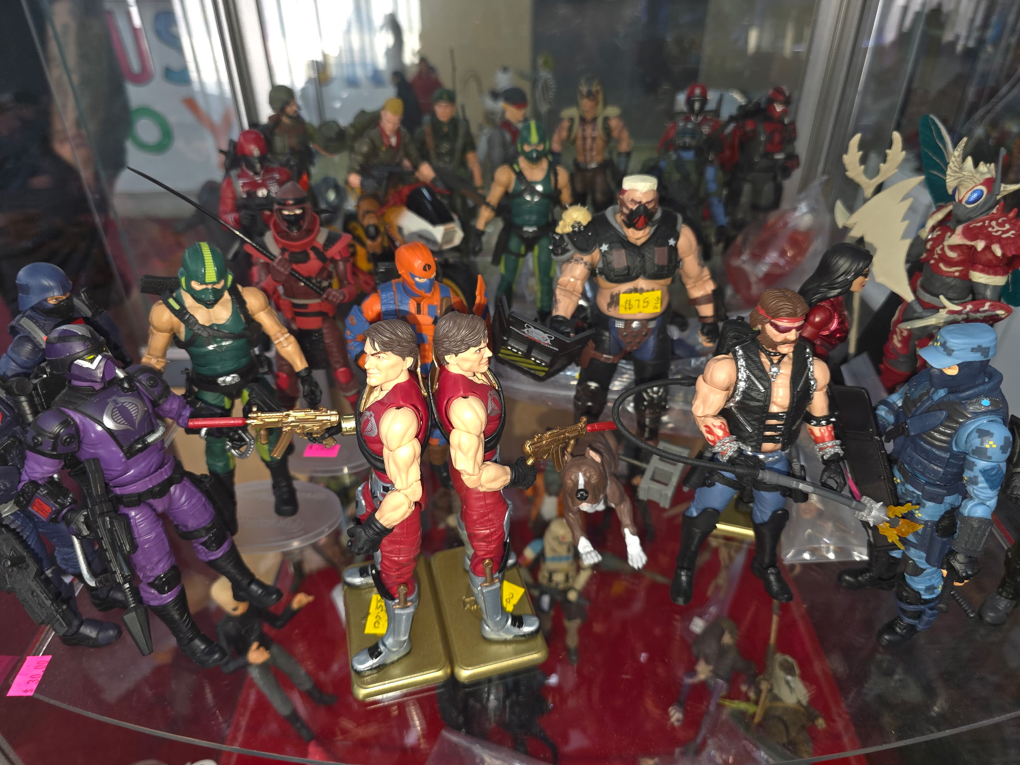 Collection of colorful action figures and toys displayed on a glass shelf, with some figures holding weapons and wearing helmets.