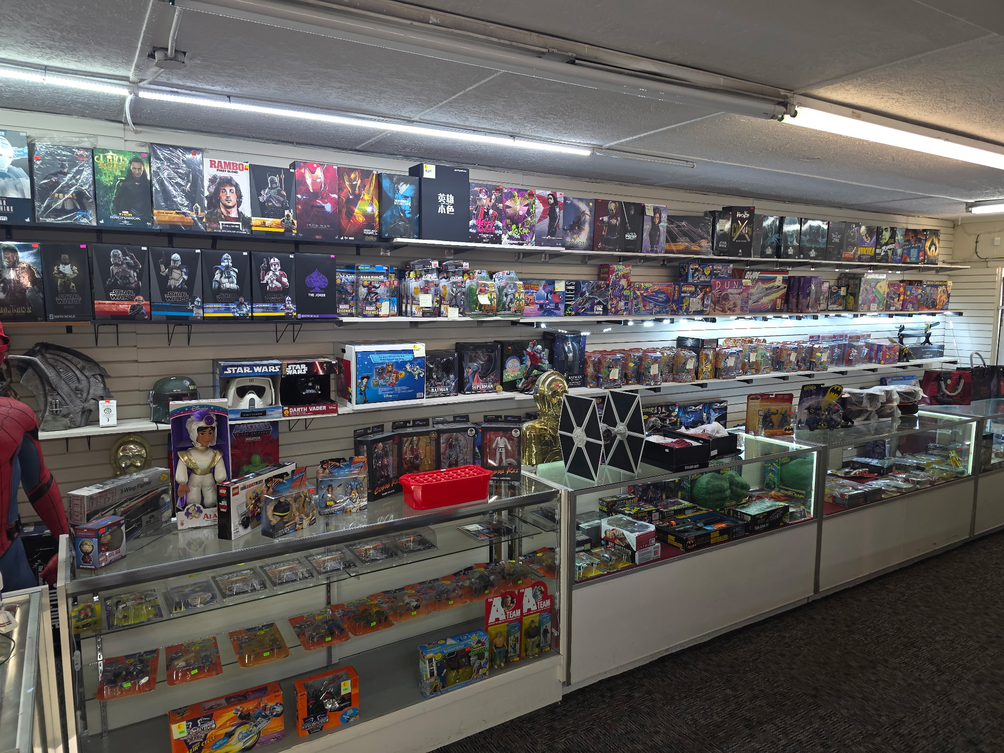 Store interior with shelves of boxed toys, collectibles, and merchandise, glass display cases, and a carpeted floor.