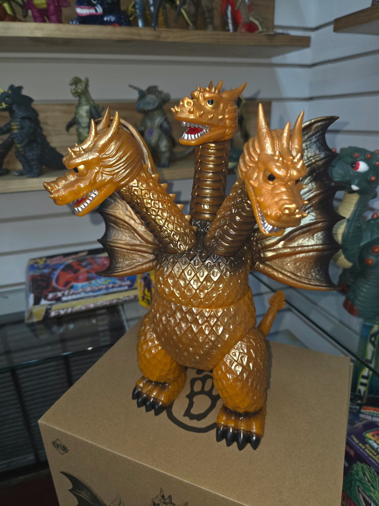 Gold-colored dragon figure with three heads, wings, and textured body, standing on a cardboard box in a store.