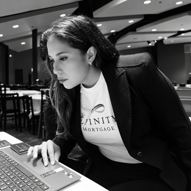 Woman with long hair looking at a laptop in a modern indoor space, wearing a blazer and a T-shirt.