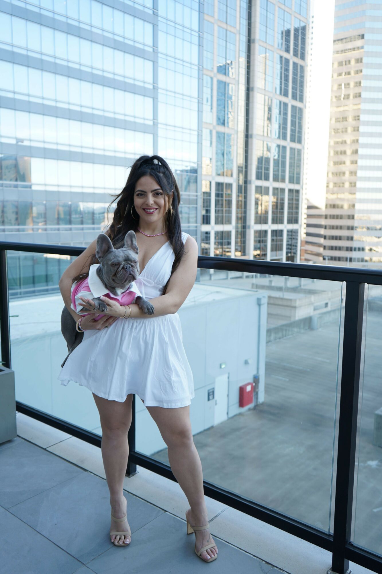 Woman holding a dog on a balcony with city buildings in the background.