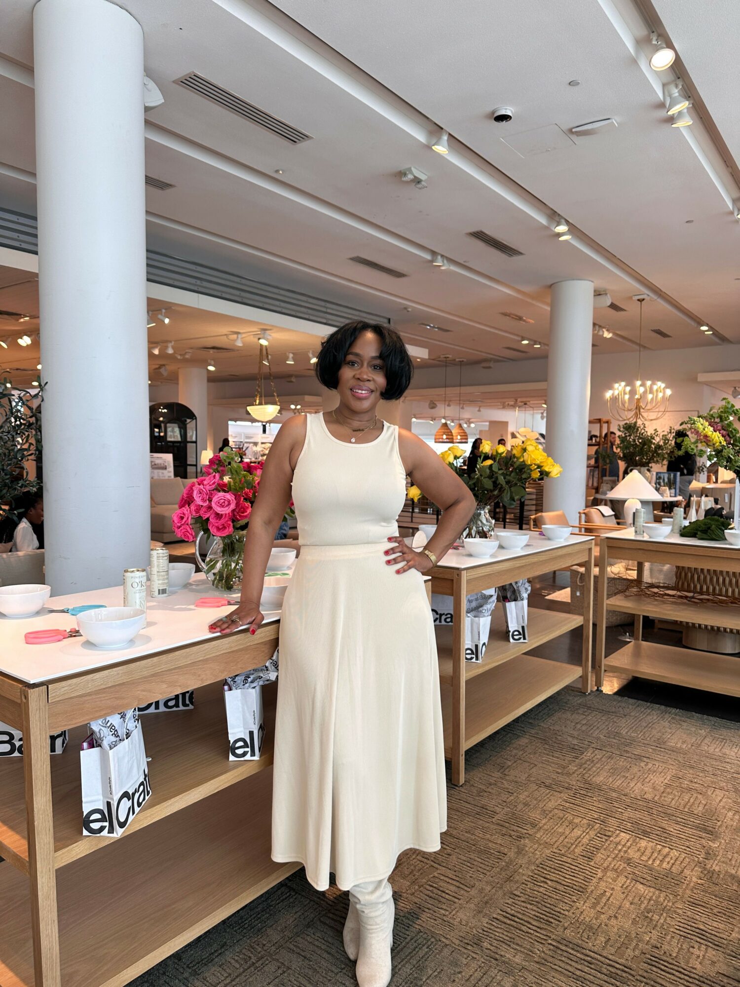 Woman in white dress standing at a table in a decorated indoor space with flowers and tables.