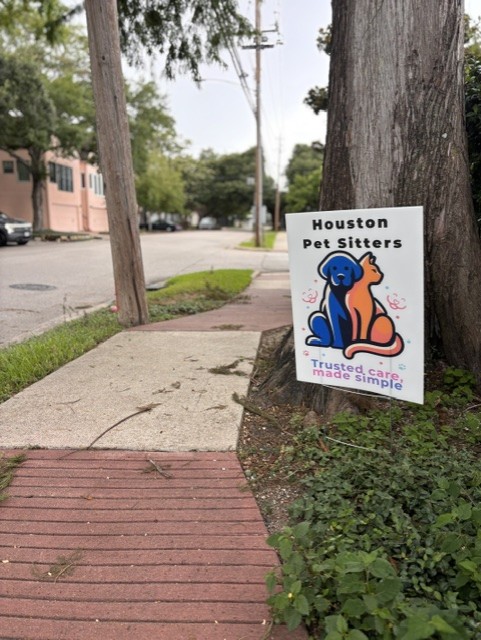 Sign on a tree advertising Houston Pet Sitters with a cartoon dog and cat, and the slogan
