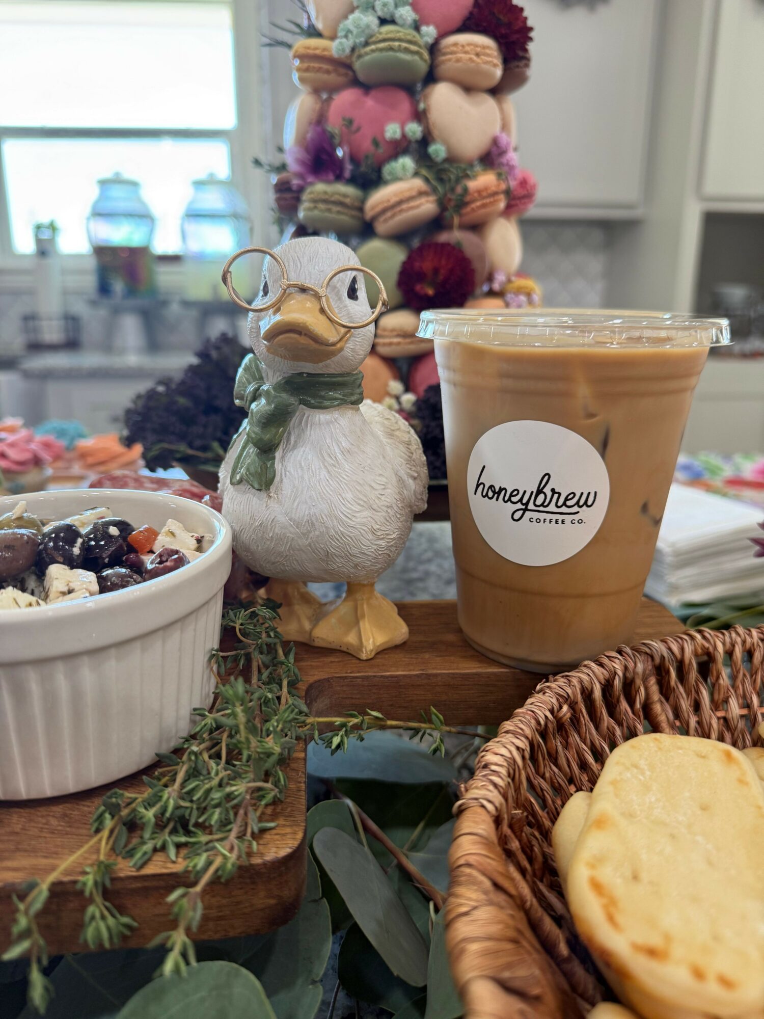 Coffee cup with a label, a bowl of berries, a basket with bread, and decorative items on a table.