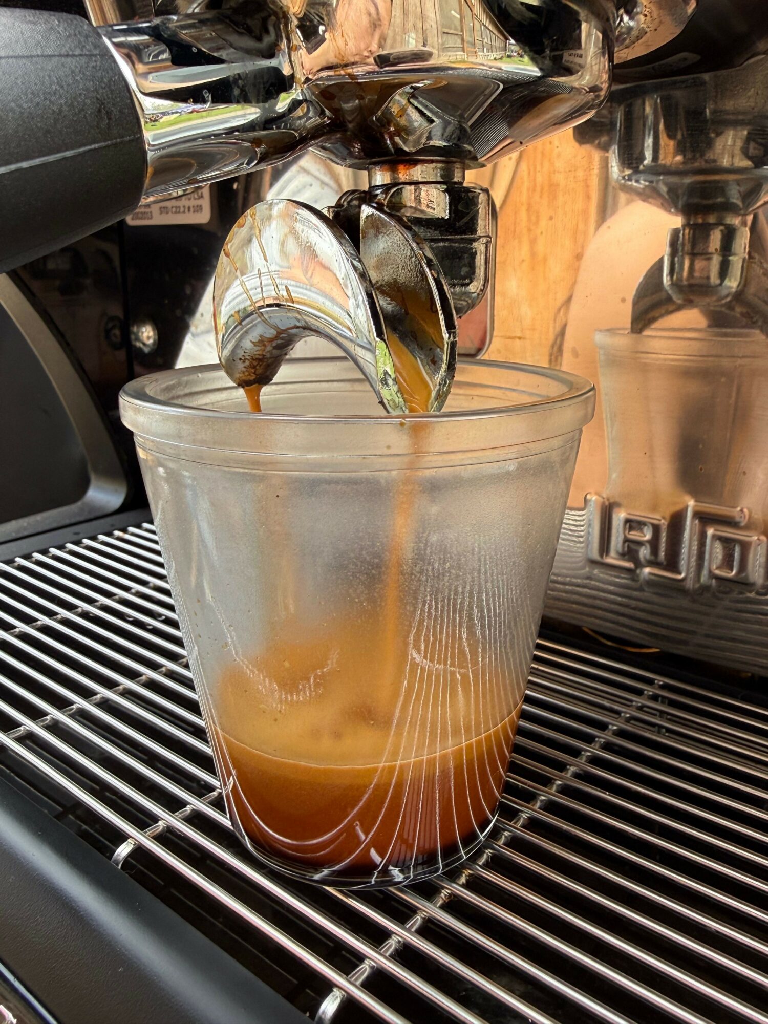 A glass of iced coffee on a metal grid surface, with a reflective metallic background.
