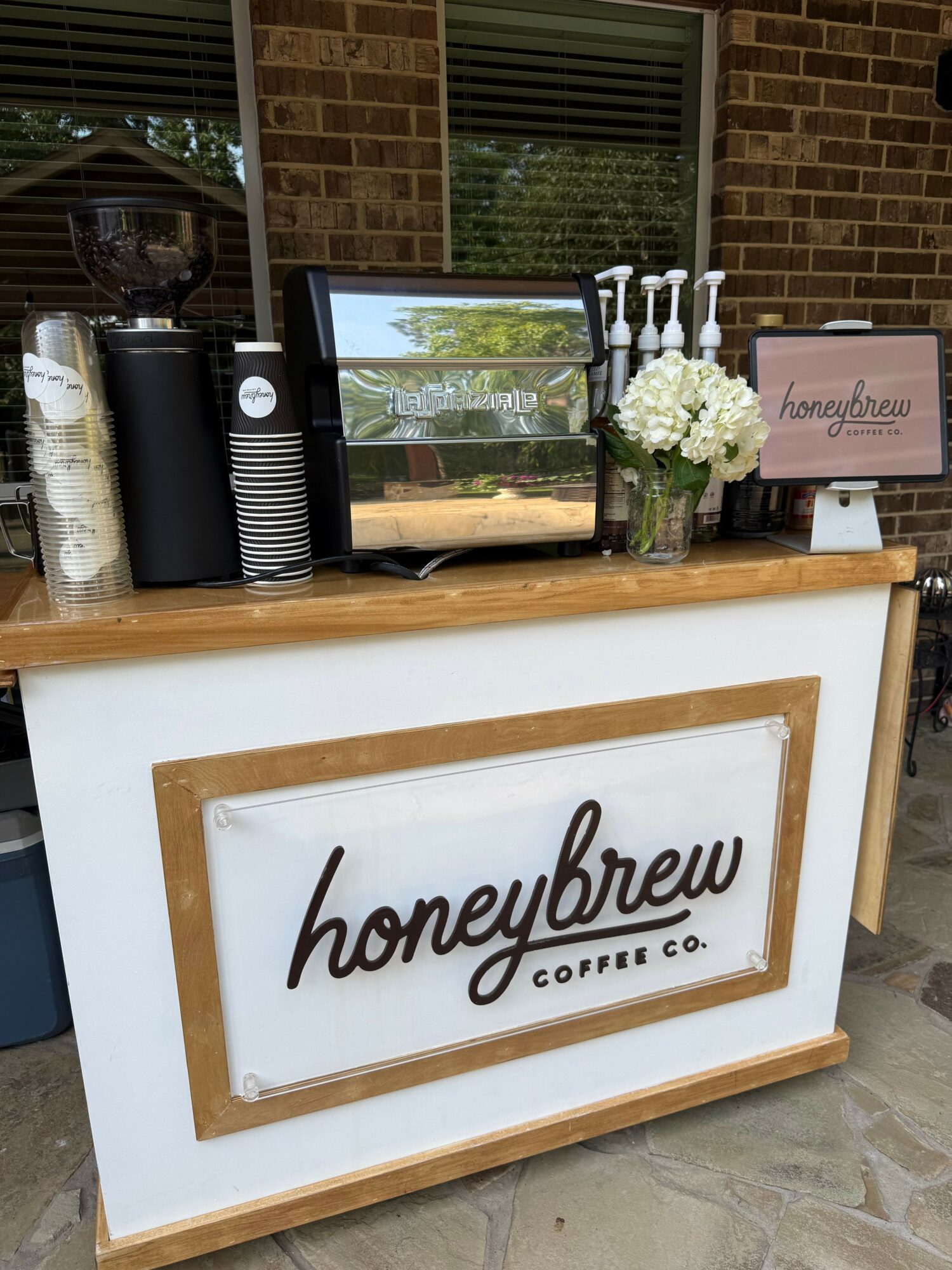 A white table with a framed sign reading 'homebrew coffee,' a flower arrangement, and coffee supplies, viewed from the side.