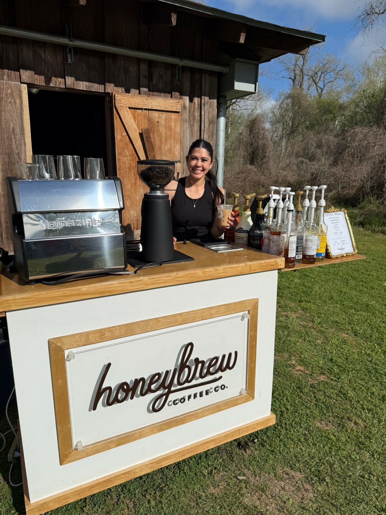 Outdoor beverage stand with bottles and a sign reading 'happy hour' on a grassy area.