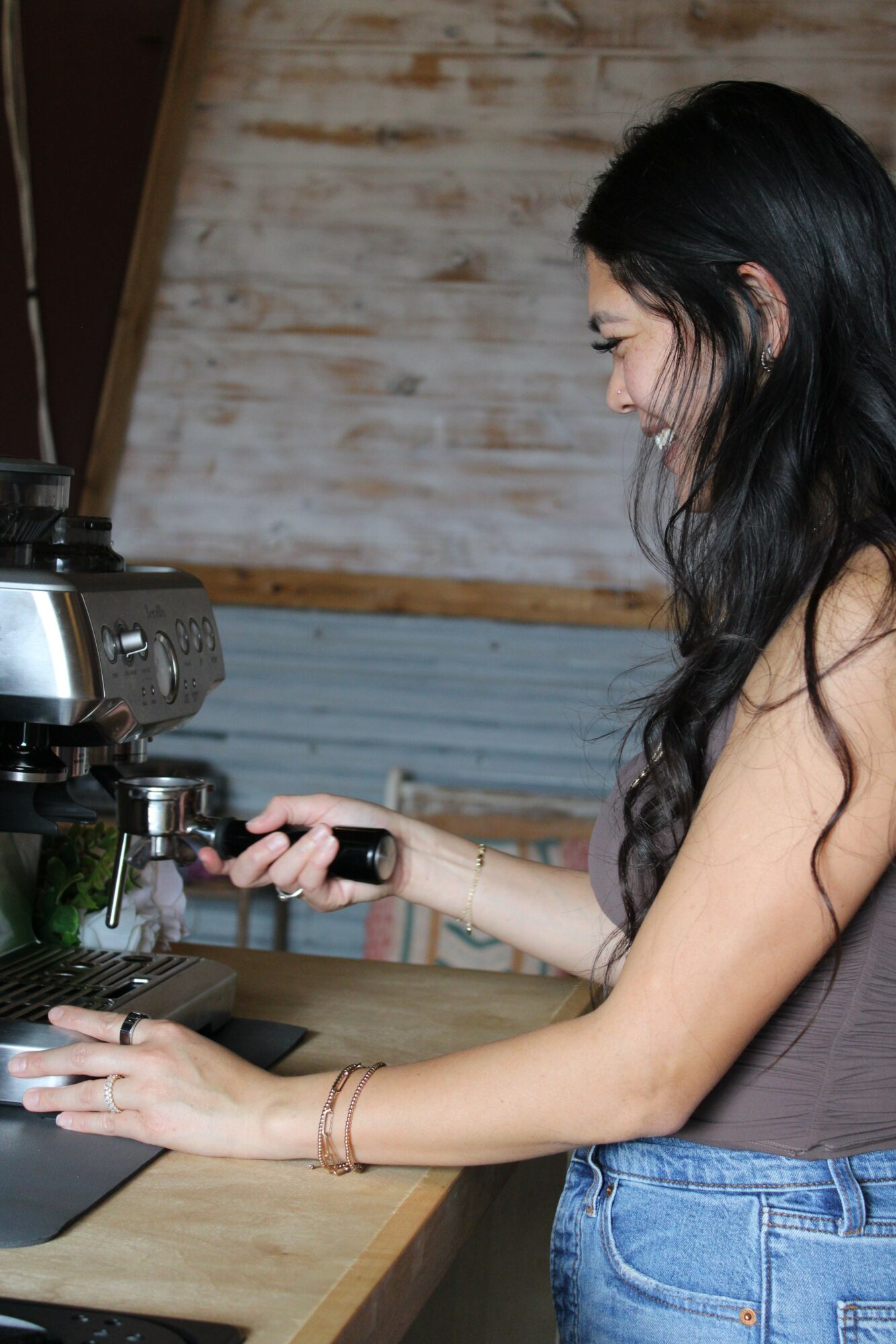 Person with long dark hair using a camera or phone to take a photo, standing at a wooden table with a rustic background.
