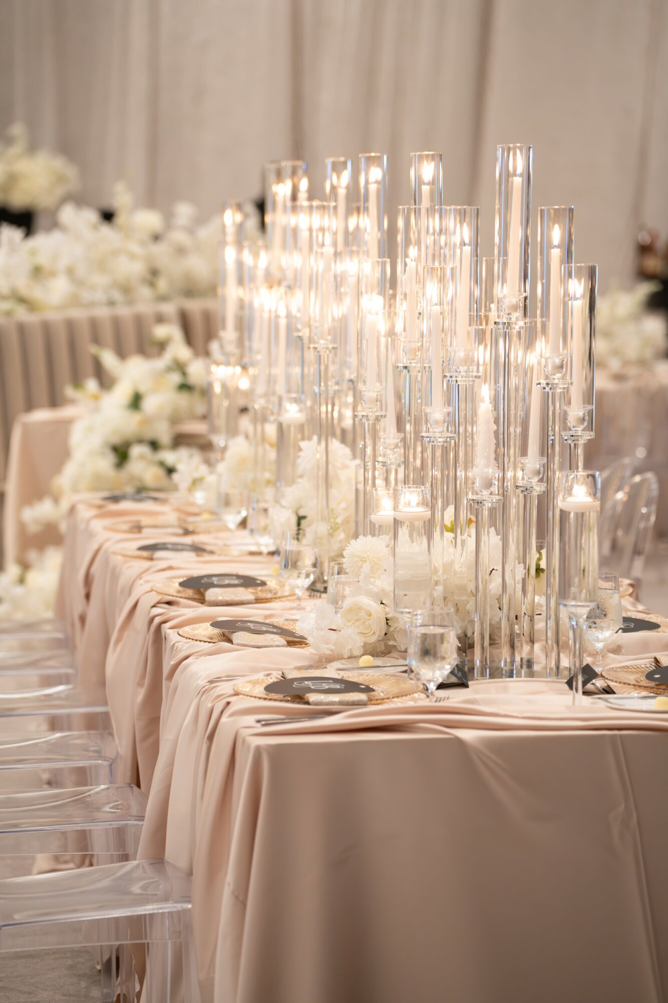 Elegant table setting with tall glass candle holders and white floral arrangements, draped tablecloth, and neatly arranged cutlery.