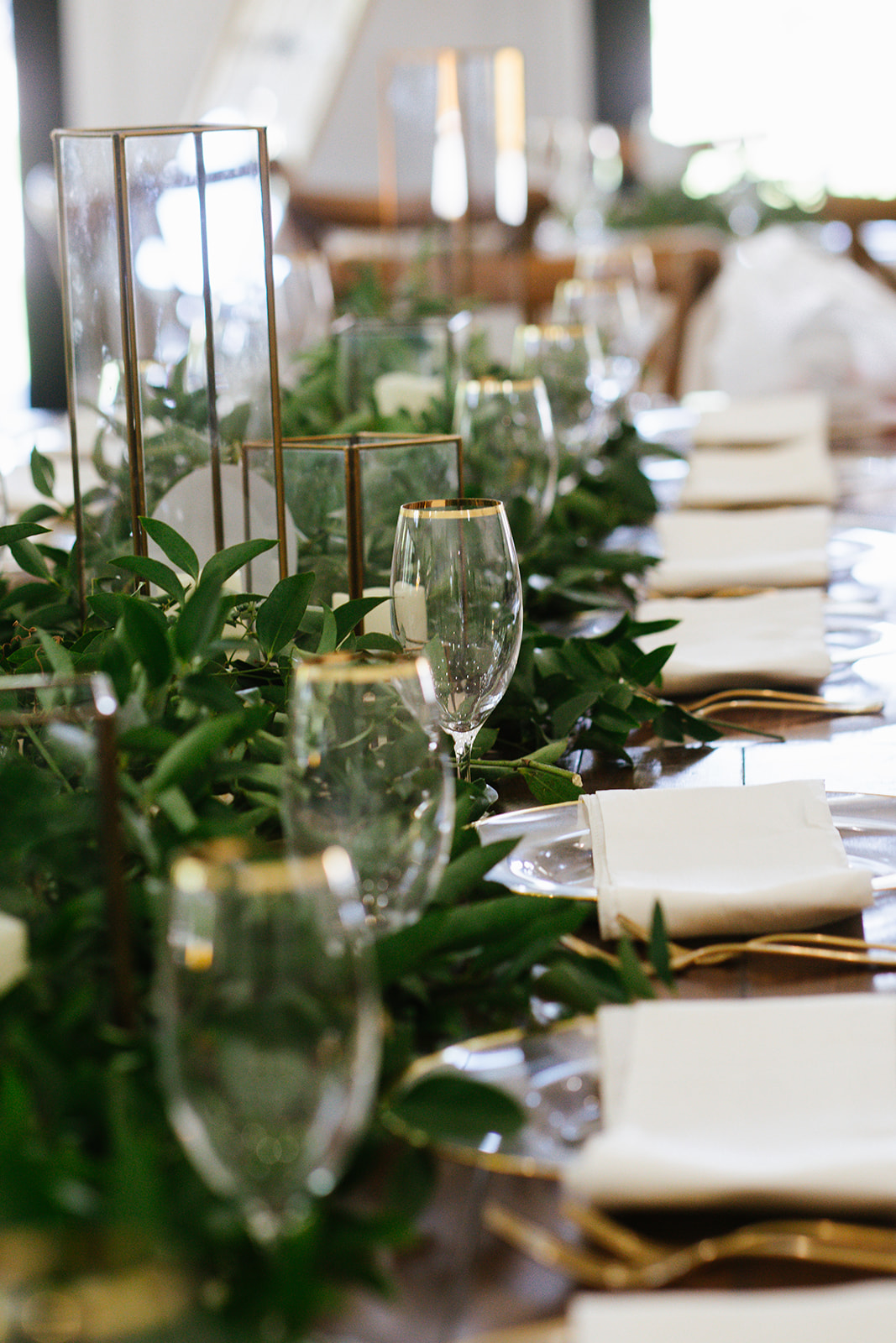 Elegant table setting with glassware, white napkins, and greenery centerpiece in a bright room.