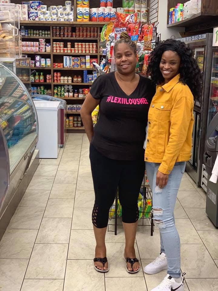 Two women standing inside a grocery store aisle, smiling, with shelves of products behind them.