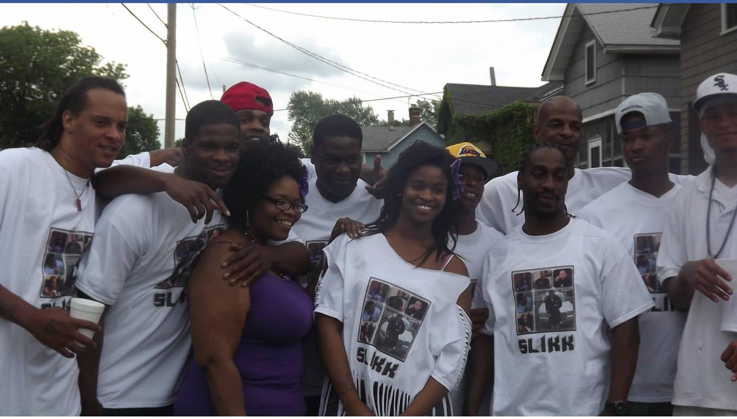 Group of people outdoors, some wearing white T-shirts with images, smiling and posing together.